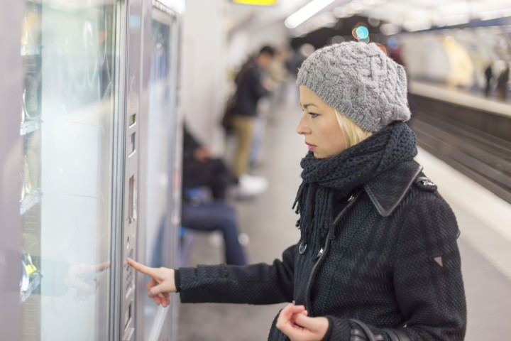 Casually dressed woman wearing winter coat,buying metro ticket at the ticket vending machine. Urban transport.