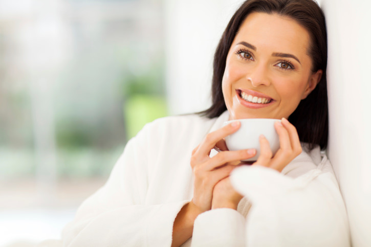 smiling woman drinking coffee on bed