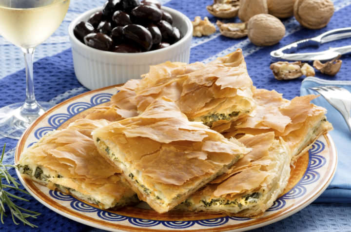 Spanakopita, Greek spinach pie with feta cheese and filo party on on plate with Greek white wine, olives and walnuts