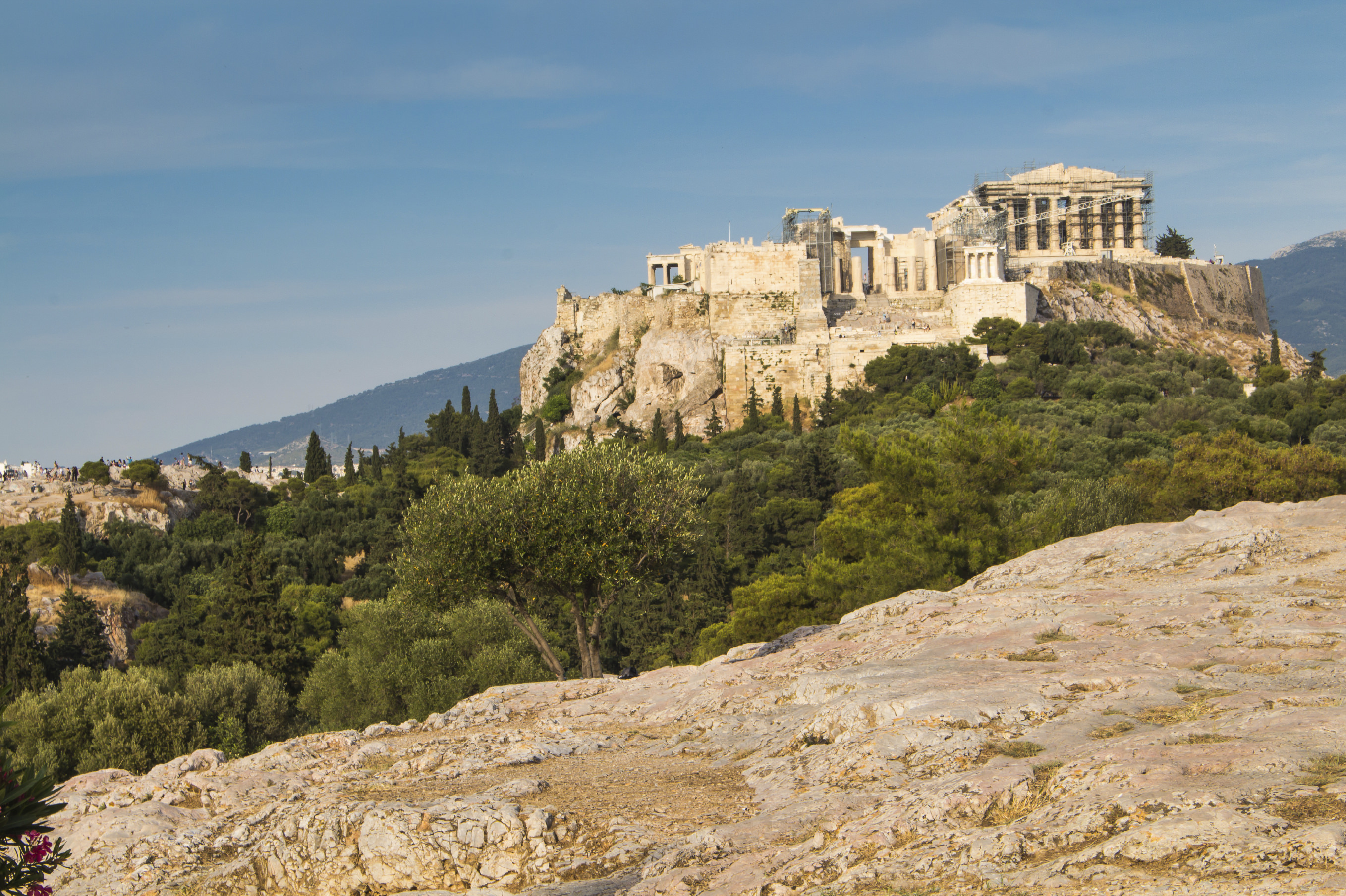 View from a park on the important greek monument: Acropolis, built on the other hill. Line of the soil with stones. Cloudy early evening sky.