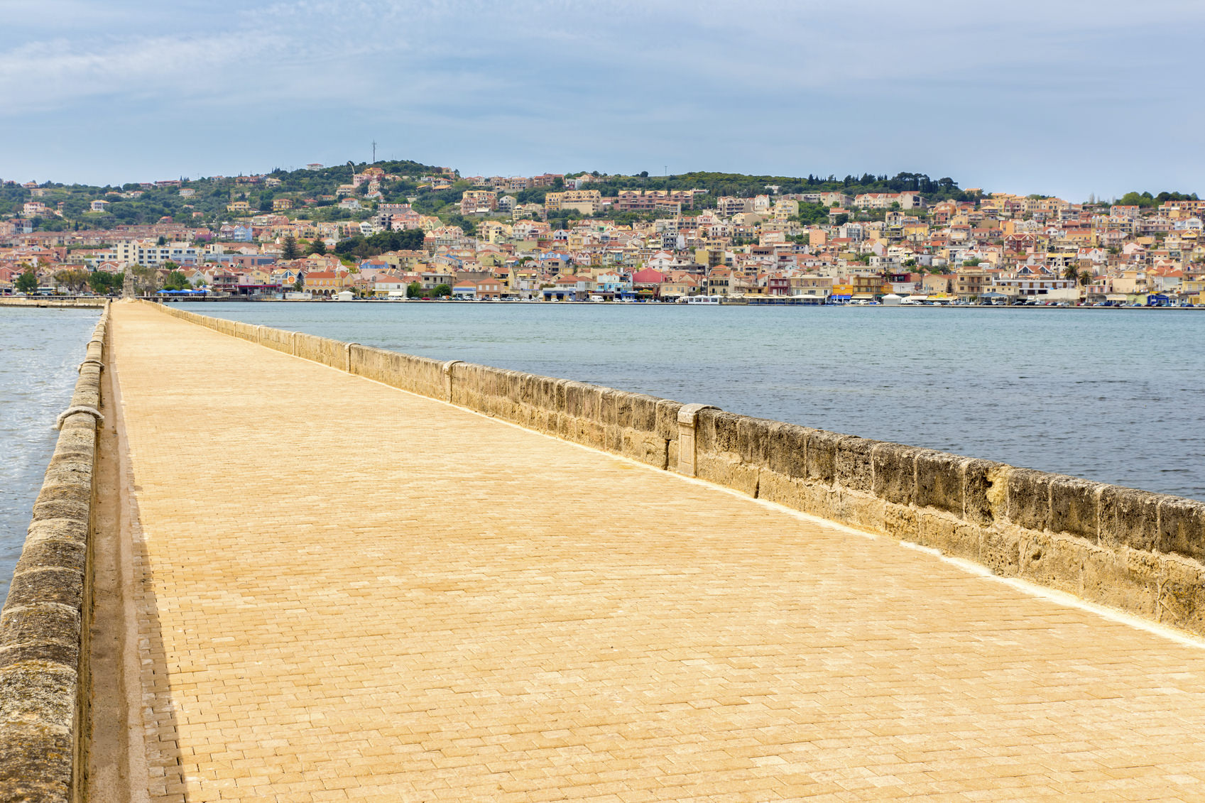 Greek City Port Argostoli with yellow road on bridge. I like this very long bridge diagonally in this photo. It's an empty road or street, no people or traffic on it. I took this photo during my vacation in Kefalonia, a greek island. In the distance you can see many houses on a mountain where the people live.