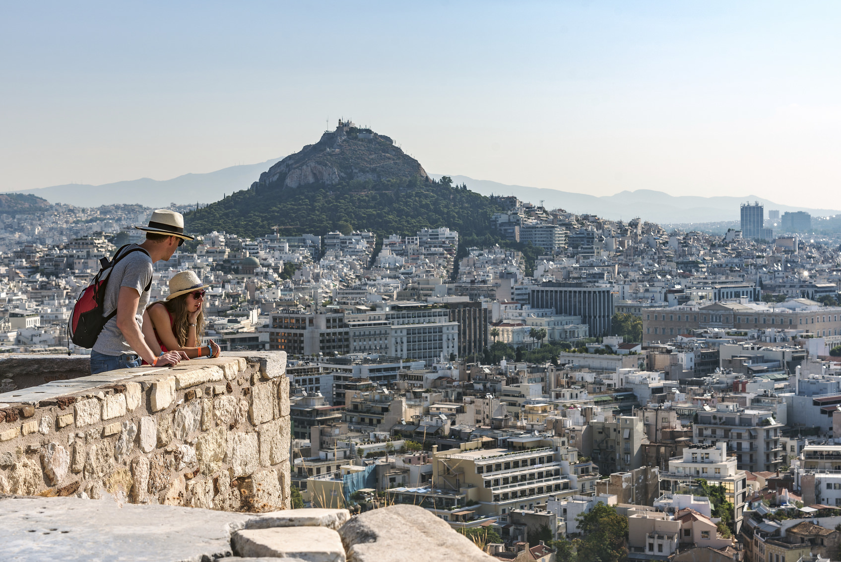 Athens, Greece - August 16, 2015: Two tourists look at panorama of Athens and Licabetus hill fro walls of Acropolis.