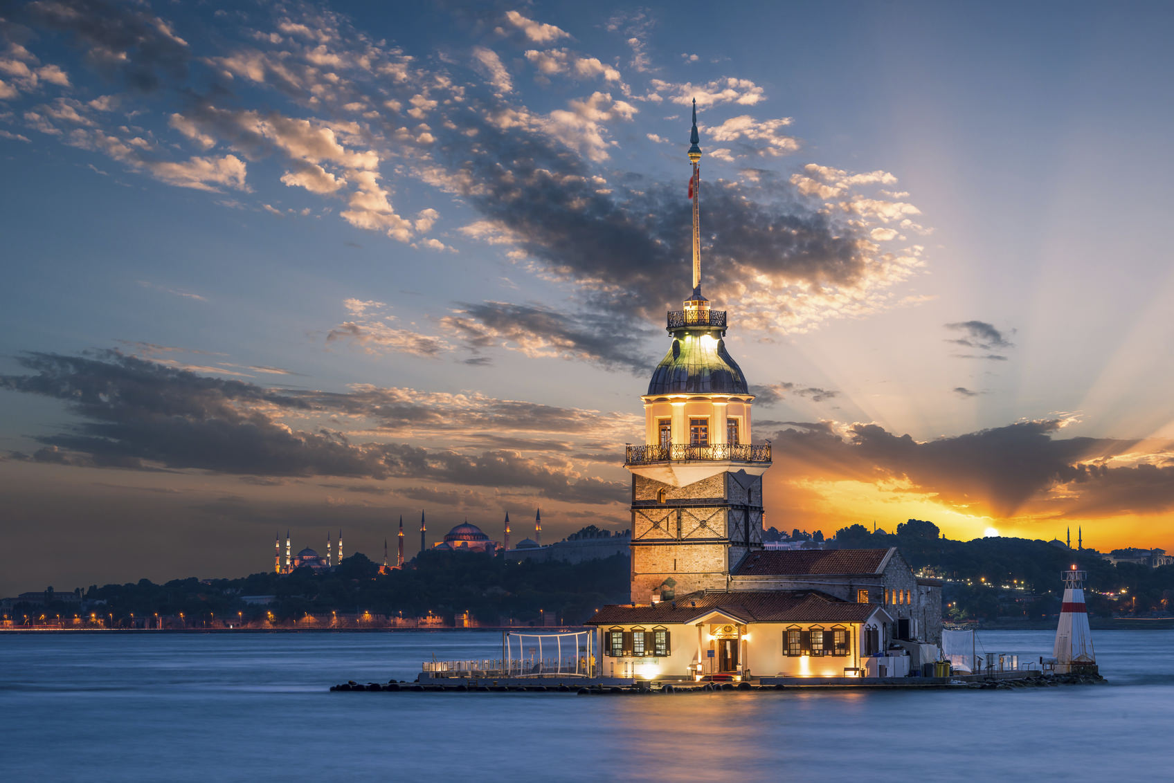 Maiden's Tower lit up in early evening, with the Hagia Sophia and the Blue Mosque in the far distance.