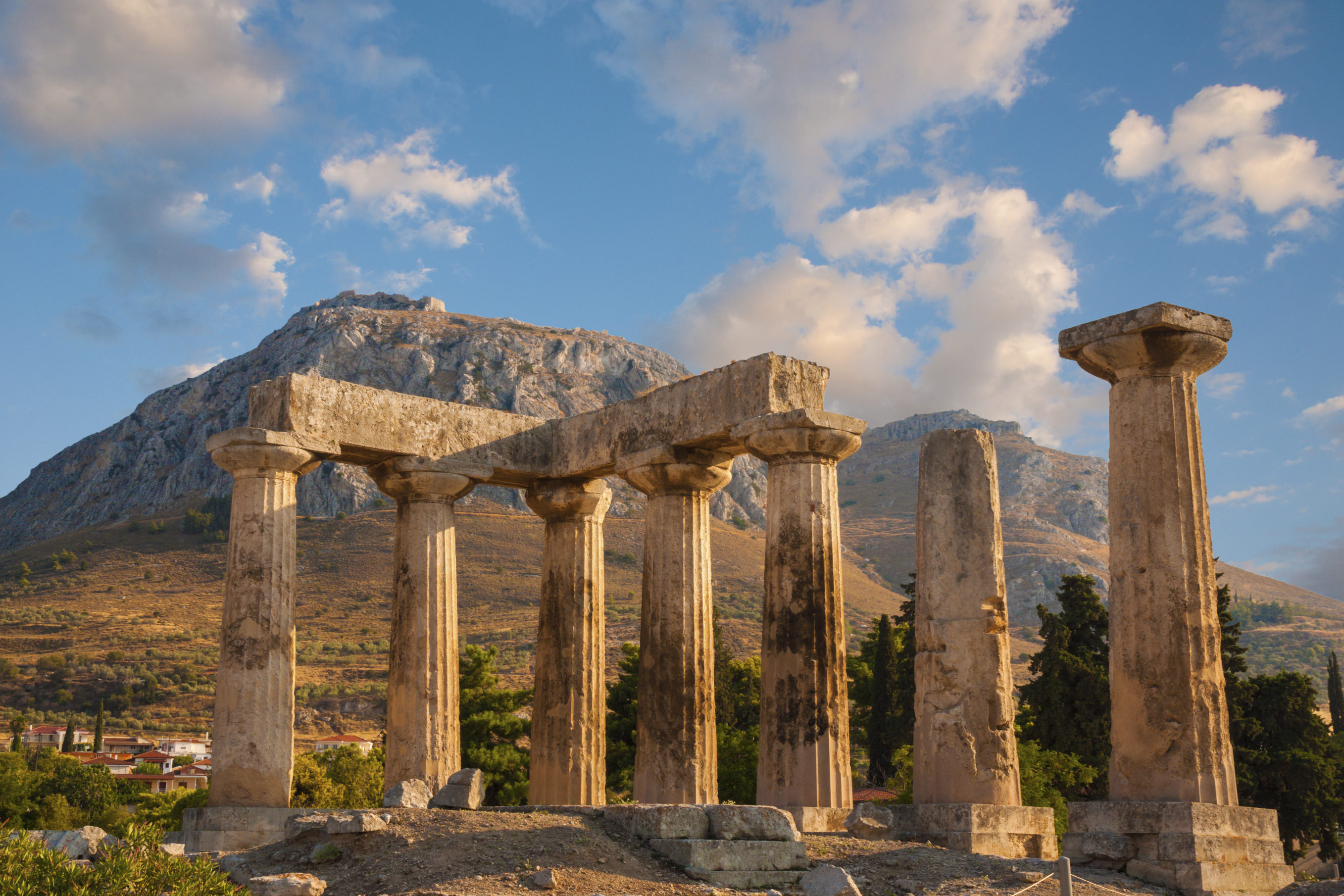 Ruins of Appollo temple with fortress at back in ancient Corinth, Greece